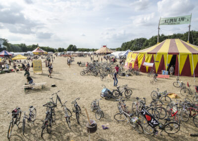 Foto von einem großen Feld, auf dem große Zelte und viele Fahrräder stehen. Dazwischen laufen Menschen lang. An einem Zelt hängt ein Banner mit "Klimacamp"