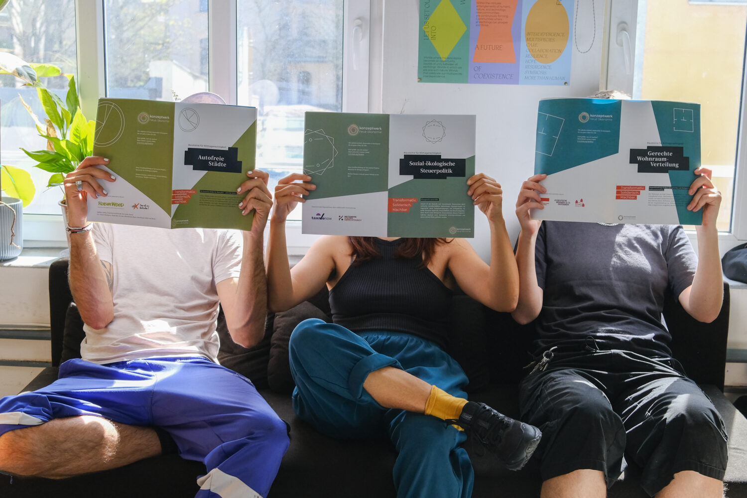 Drei Personen sitzen auf dem Sofa und haben jeweils ein aufgeschlagenes Heft vor sich
