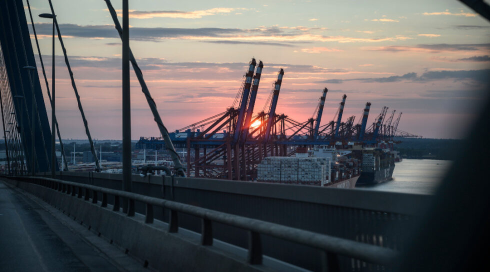 Ein LNG Terminal mit zwei Frachterschiffen davor, im Hintergrund geht die Sonne auf