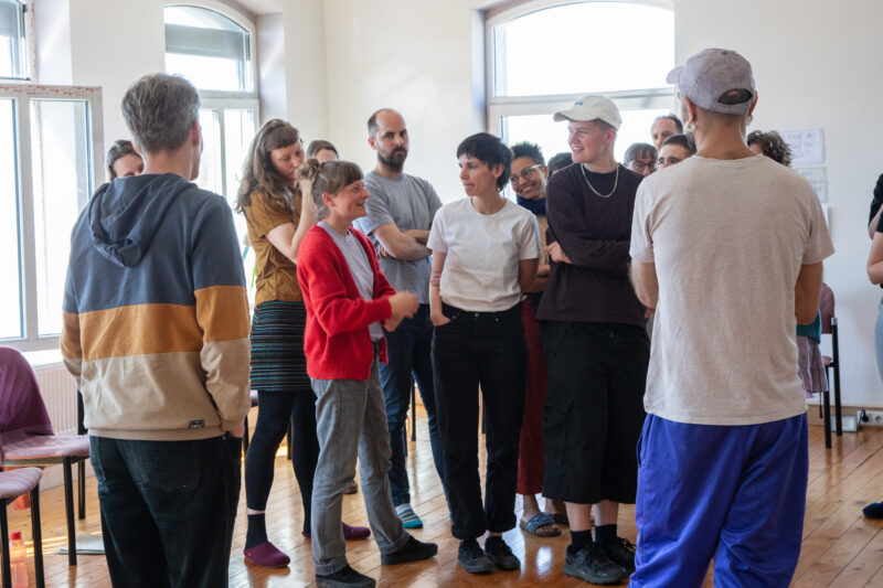 Eine Gruppe von etwa 20 Menschen zwischen 25 und 40 stehen zusammen und diskutieren mit entspanntem Gesichtsausdruck