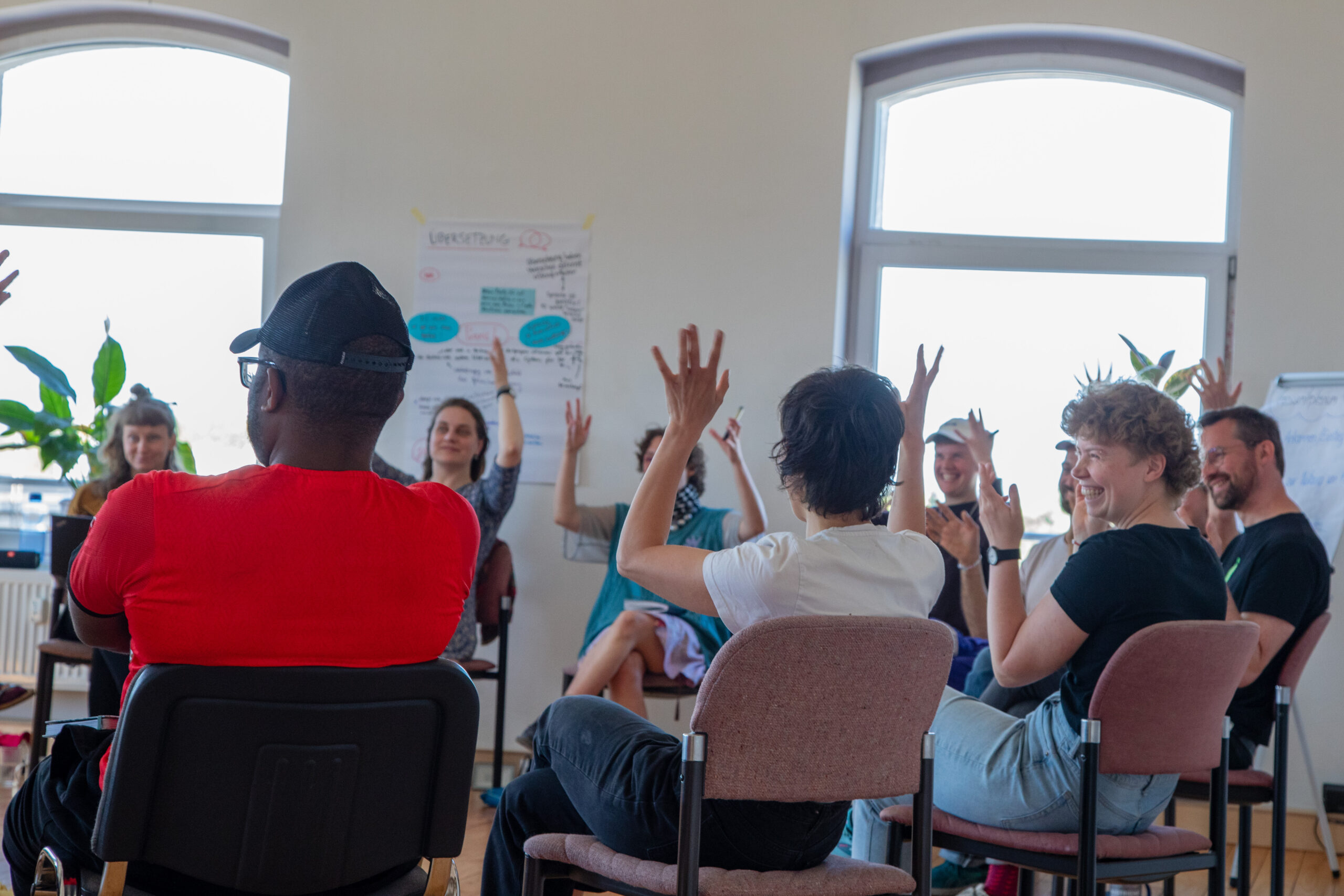 Viele Menschen sitzen im Kreis zusammen und stimmen mit den Händen ab und lächeln sich an