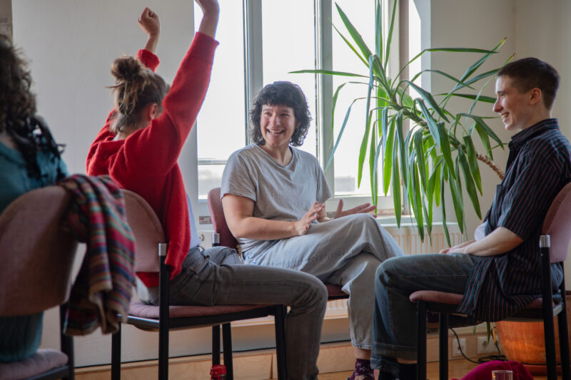 Drei Personen sitzen im Besprechungsraum zusammen und freuen sich gemeinsam, eine Person reißt die Arme nach oben