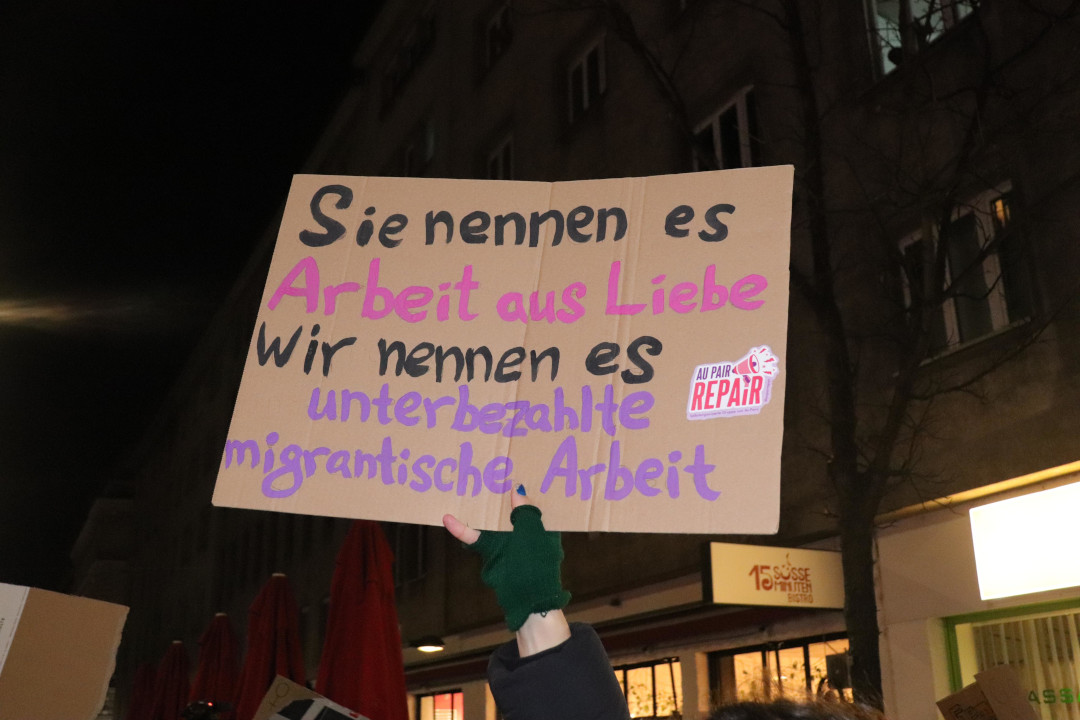 Pappschild mit handgeschriebener Aufschrift: Sie nennen es Arbeit aus Liebe, wir nennen es unterbezhalte migrantische Arbeit